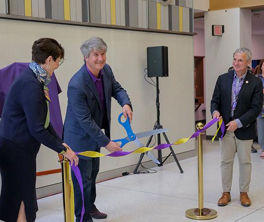 three people, two men and a women, one cutting a ribbon